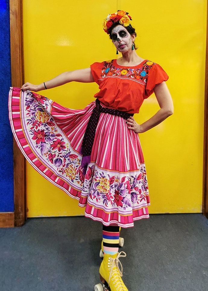 woman wearing rollerskates, mexican clothing with dia del los muertos skull face paint and floral headband