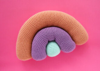crochet rainbow cushion on pink background