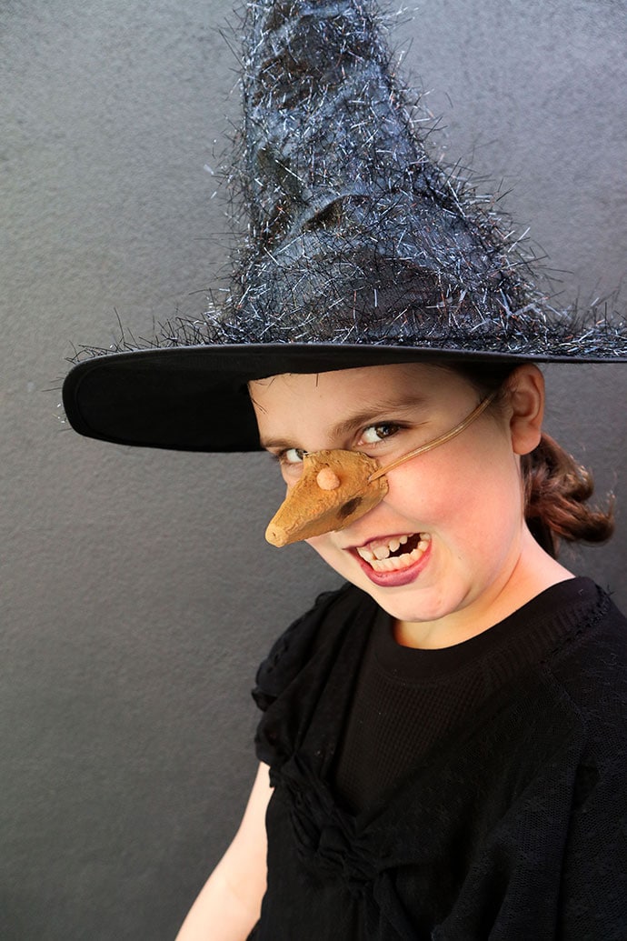 Girl wearing fake witch nose and black hat