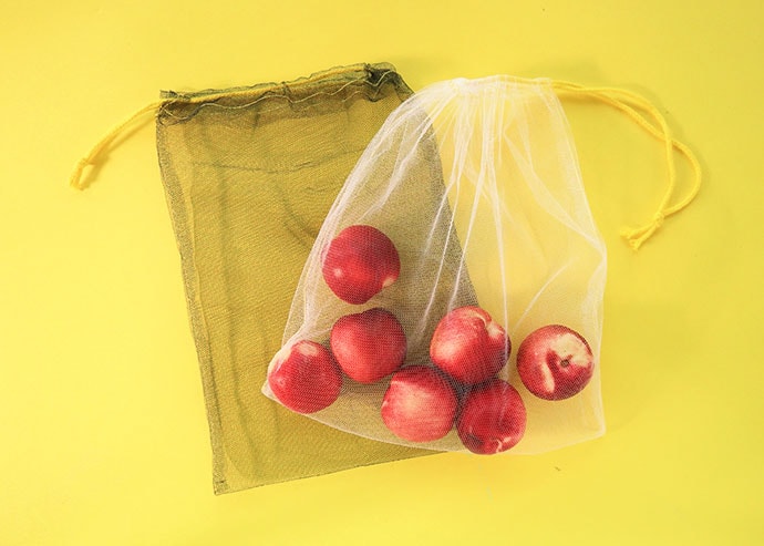 Mesh produce bags filled with fruit on yellow background