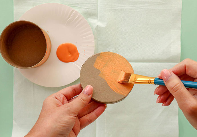 Hands painting a round box lid with peach colored paint