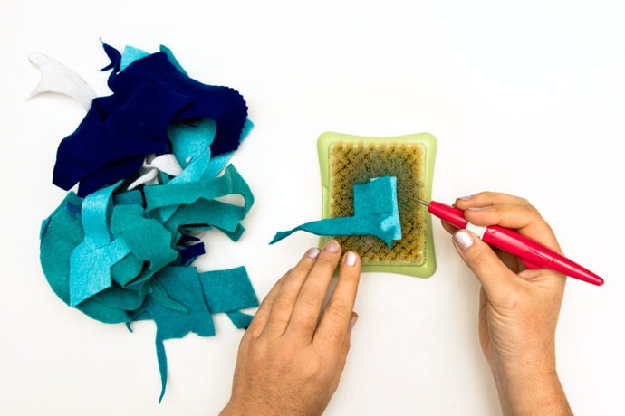 hands using needle felt tools to felt together scrap felt pieces