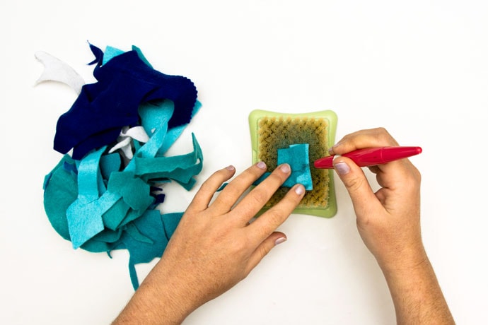 hands using needle felt tools to felt together scrap felt pieces