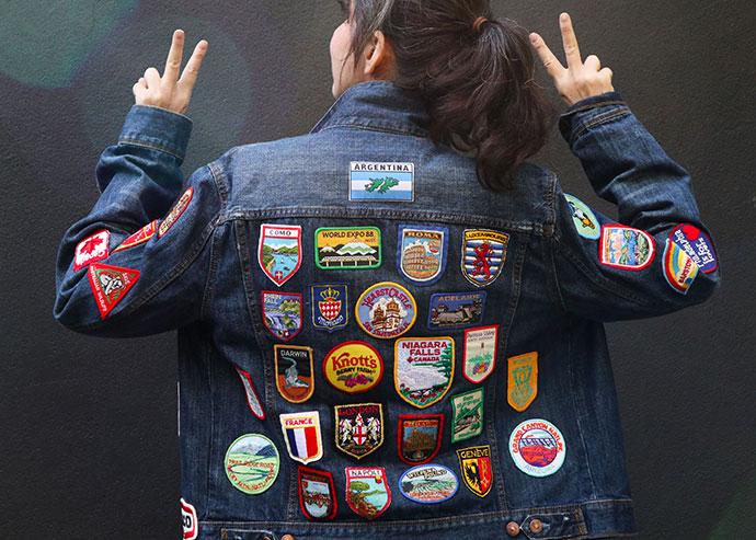 woman wearing denim jacket back covered in vintage travel patches