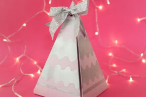 Pyramid shaped christmas gift box with silver bow on pink background