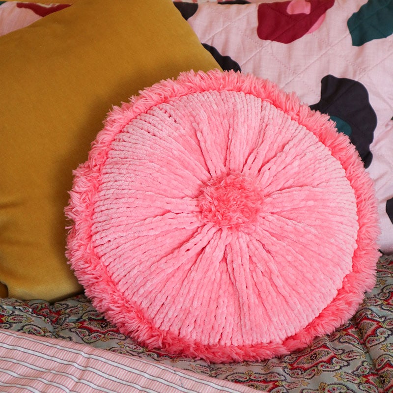 round pink knitted throw pillow on a bed